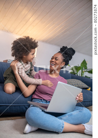 Cheerful mom with laptop and little girl demanding attention Cheerful mom with laptop and little girl demanding attention 80273874