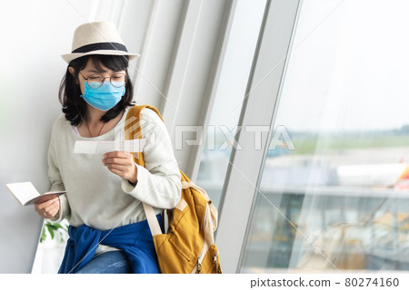 Asian Female tourist wearing protective face mask holding boarding pass Asian Female tourist wearing protective face mask holding boarding pass 80274160