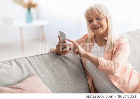 Smiling mature woman using mobile phone resting on sofa 80275551
