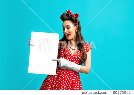 Excited pinup retro style woman pointing at empty advertising banner with copy space on blue studio background, mockup Excited pinup retro style woman pointing at empty advertising banner with copy space on blue studio background, mockup 80275962