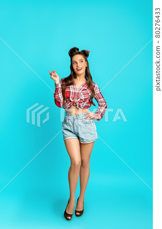 Full length portrait of playful happy pinup woman in retro style wear posing over blue studio background 80276433