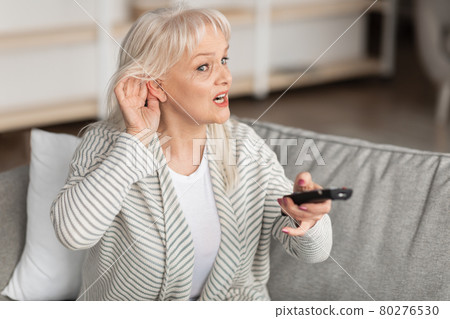 Hearing Problems. Mature woman watching television sitting on couch Hearing Problems. Mature woman watching television sitting on couch 80276530