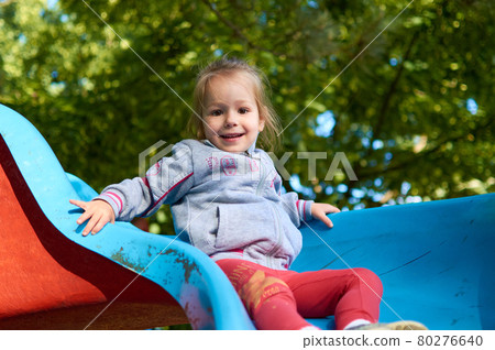 Cute little girl having fun while sliding down a playground slide Cute little girl having fun while sliding down a playground slide 80276640