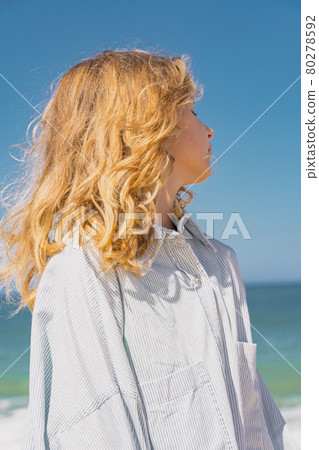Young beautiful girl in blue dress staying along the sandy beach near the waves. 80278592