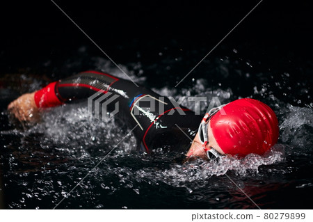triathlon athlete swimming in dark night wearing wetsuit 80279899