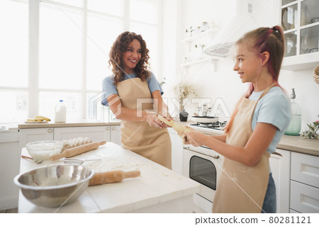 Teen girl helping her mom to cook dough in their kitchen at home Teen girl helping her mom to cook dough in their kitchen at home 80281121