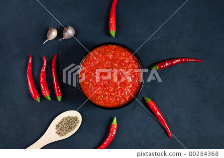 Hot chili pepper sauce paste harissa. Adjika on a blue background. Traditional Tunisia, Georgian and Arabic cuisine. Homemade rose harissa in a bowl. 80284368