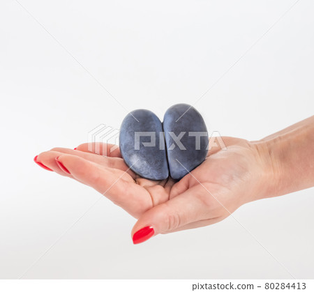 Trendy ugly food concept. Purple ugly plum in a woman's hand on a white background. Fruit with heart shape. The problem of food waste Trendy ugly food concept. Purple ugly plum in a woman's hand on a white background. Fruit with heart shape. The problem of food waste 80284413