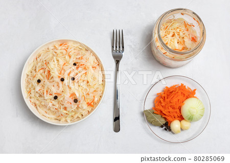 Homemade sauerkraut. Fermented food. Sauerkraut with carrots in a bowl and glass jar on a concrete white background. Vertical orientation. Homemade sauerkraut. Fermented food. Sauerkraut with carrots in a bowl and glass jar on a concrete white background. Vertical orientation. 80285069
