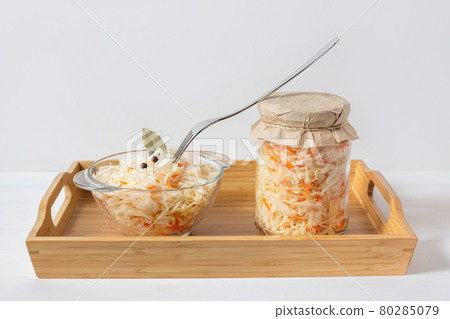Homemade sauerkraut. Fermented food. Sauerkraut with carrots in a glass jar and bowl in a wooden tray on a white background Homemade sauerkraut. Fermented food. Sauerkraut with carrots in a glass jar and bowl in a wooden tray on a white background 80285079