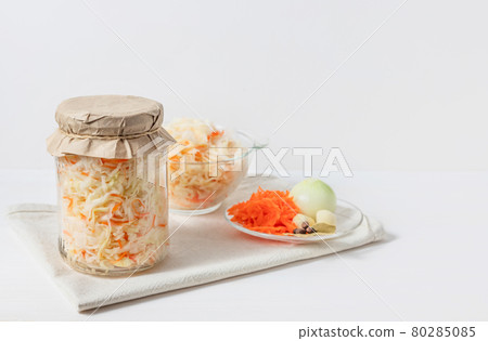 Homemade sauerkraut with carrots in a glass jar and bowl on a white wooden background. Fermented food. Homemade sauerkraut with carrots in a glass jar and bowl on a white wooden background. Fermented food. 80285085