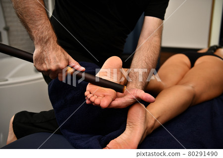 Close up of therapist hands massaging female legs with bamboo stick. Thai foot massage at the spa salon Close up of therapist hands massaging female legs with bamboo stick. Thai foot massage at the spa salon 80291490