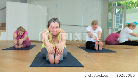 Ladies are doing seating forward bend Ladies are doing seating forward bend 80293099