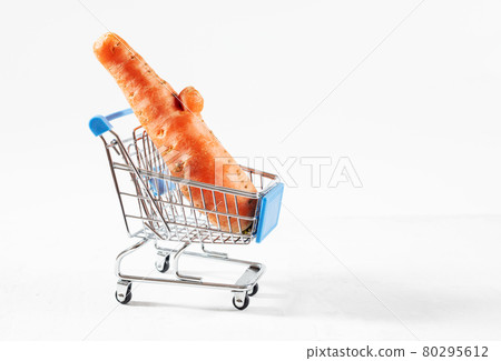 Trendy ugly food concept. Funny carrot in toy grocery cart on white background. Vegetable with a strange shape. The problem of food waste. Trendy ugly food concept. Funny carrot in toy grocery cart on white background. Vegetable with a strange shape. The problem of food waste. 80295612