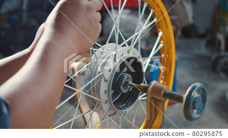Technician man working motorcycle wheel has spokes weave up on mechanic tool new steel wheel 80295875