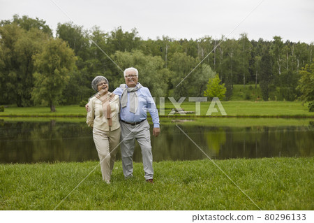 An elderly couple in casual clothes are walking outdoors 80296133