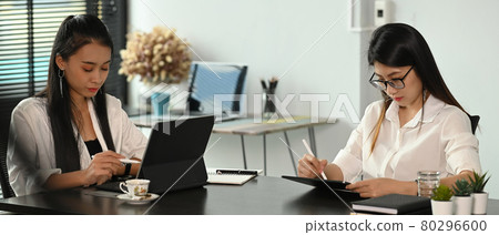 Two businesswoman are working together at a boardroom table during a meeting in a modern office. Two businesswoman are working together at a boardroom table during a meeting in a modern office. 80296600