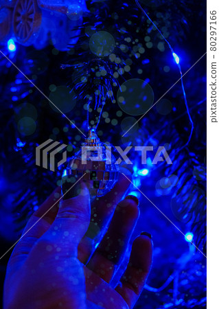 Female hand holding christmas tree decorations at night. Bright garland blue light. New Year magic moments. Fairytale 80297166