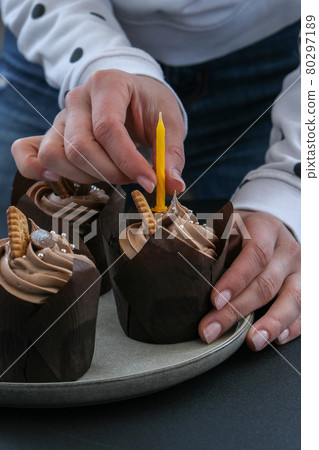 Female hands making Delicious chocolate cupcakes with cream on dark background. Three chocolate muffin. Birthday cake party preparation Female hands making Delicious chocolate cupcakes with cream on dark background. Three chocolate muffin. Birthday cake party preparation 80297189