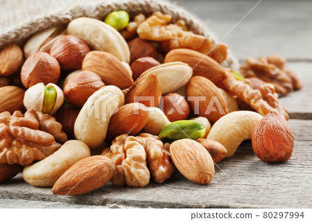 A mixture of fresh nuts spilled from a linen bag onto a gray wooden table. A mixture of fresh nuts spilled from a linen bag onto a gray wooden table. 80297994