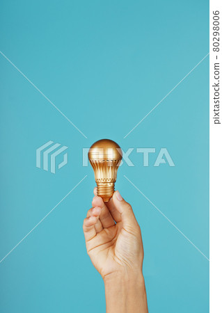 Gold light bulb in hand on a blue background, as a concept of ideas and assistance Gold light bulb in hand on a blue background, as a concept of ideas and assistance 80298006