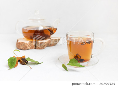 Chaga tea in a glass mug and teapot on a white background. Trendy healthy beverage. Drink with pieces of birch mushroom. Chaga tea in a glass mug and teapot on a white background. Trendy healthy beverage. Drink with pieces of birch mushroom. 80299585