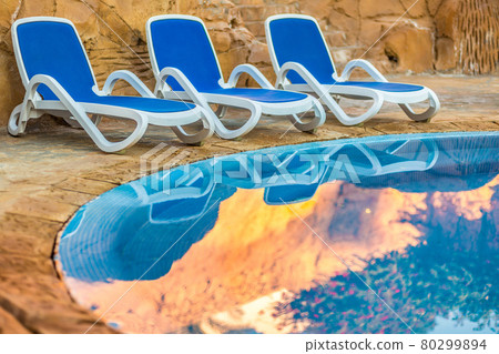 Three sunloungers reflected in blue water of the swimming pool 80299894