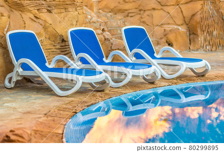 Sunloungers near swimming pool and reflected their in blue water 80299895