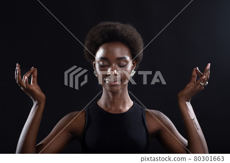 Studio portrait of african american female model showing zen or okay sign gesture. Woman meditating on black background. Studio portrait of african american female model showing zen or okay sign gesture. Woman meditating on black background. 80301663