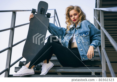 Beautiful adorable young girl in retro 90s fashion style, outfits posing on stairs, outdoors. Concept of eras comparison, beauty, fashion and youth. Beautiful adorable young girl in retro 90s fashion style, outfits posing on stairs, outdoors. Concept of eras comparison, beauty, fashion and youth. 80302323
