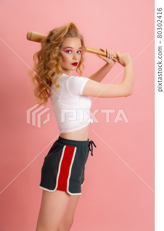Beautiful young girl with bright makeup and hairdo in retro 90s fashion style in image of Harley Quinn isolated over pink studio background. Concept of eras comparison 80302416