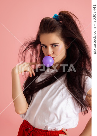 Portrait of adorable pretty young girl in retro 90s fashion style, outfits posing isolated over pink studio background. Concept of eras comparison, beauty, fashion and youth. Portrait of adorable pretty young girl in retro 90s fashion style, outfits posing isolated over pink studio background. Concept of eras comparison, beauty, fashion and youth. 80302441