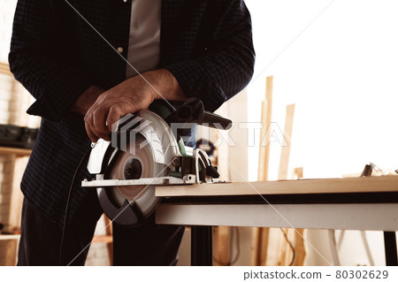 Carpenter hands cutting wood with electrical saw 80302629