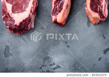Raw prime beef meat dry aged steak, tomahawk, t bone or porterhouse and club steak, on gray stone background, top view flat lay, with copy space for text 80302879