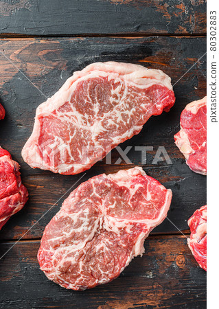 Variety of organic raw beef steakes, top blade cut on old rustic dark wooden background, top view. Variety of organic raw beef steakes, top blade cut on old rustic dark wooden background, top view. 80302883