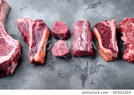 Fresh raw Prime Black Angus beef marbled and dry aged steaks, tomahawk, t bone, club steak, rib eye and tenderloin cuts, on gray stone background, with copy space for text Fresh raw Prime Black Angus beef marbled and dry aged steaks, tomahawk, t bone, club steak, rib eye and tenderloin cuts, on gray stone background, with copy space for text 80302884