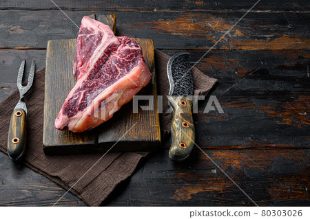 Raw fresh dry aged beef T-bone steak, on wooden cutting board, on old dark wooden table background, with copy space for text Raw fresh dry aged beef T-bone steak, on wooden cutting board, on old dark wooden table background, with copy space for text 80303026