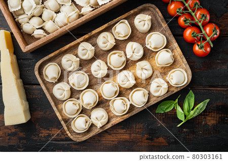 Raw Italian ravioli tortellini with fresh parmesan and basil , tomatoes on old dark wooden table background , top view flat lay 80303161