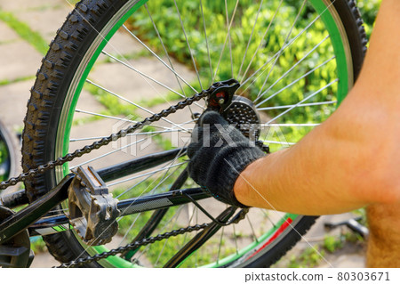 Bike mechanic man repairs bicycle in bicycle repair shop, outdoor. Hand of cyclist bicyclist examines, fixes modern cycle transmission system. Bike maintenance, sport shop concept. 80303671