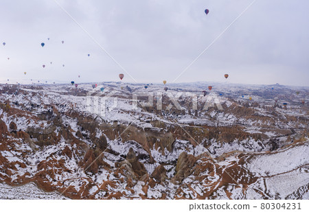 CAPPADOCIA, TURKEY - APRIL 10, 2021: Hot-air balloons in Snowy Cappadocia in Winter Morning. Turkey CAPPADOCIA, TURKEY - APRIL 10, 2021: Hot-air balloons in Snowy Cappadocia in Winter Morning. Turkey 80304231