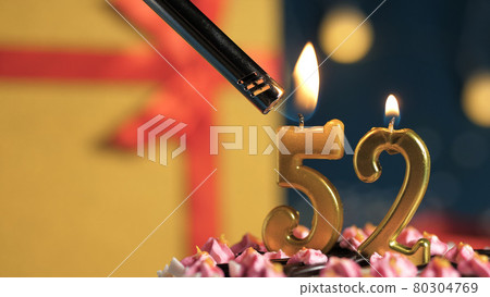 Birthday cake number 52 golden candles burning by lighter, background gift yellow box tied up with red ribbon. Close-up 80304769