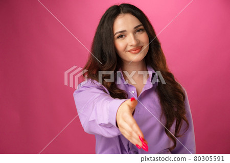 Young brunette woman giving hand for handshake against pink background Young brunette woman giving hand for handshake against pink background 80305591