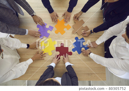 Business team standing around an office table trying to match pieces of a jigsaw puzzle 80305752