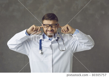 Annoyed stressed doctor closes ears with fingers trying to ignore loud hospital noises Annoyed stressed doctor closes ears with fingers trying to ignore loud hospital noises 80305757