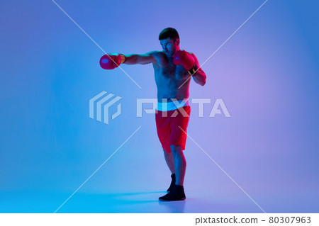 Caucasian man, professional boxer in sportwear boxing on studio background in gradient neon light. Concept of sport, activity, movement, wellbeing. 80307963
