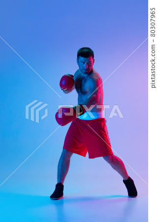 One man, professional boxer in sportwear boxing on studio background in gradient neon light. Concept of sport, activity, movement, wellbeing. One man, professional boxer in sportwear boxing on studio background in gradient neon light. Concept of sport, activity, movement, wellbeing. 80307965
