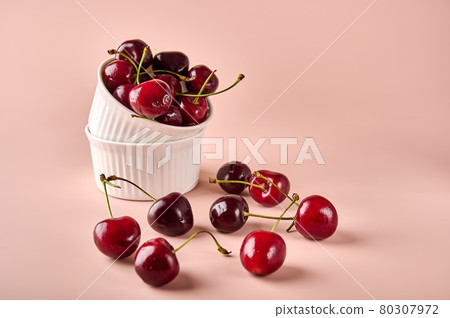Ripe red wet cherry in white bowl and next to it on powdery pink background 80307972