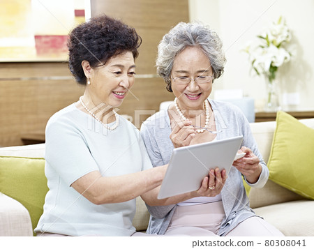 two senior asian women sitting on couch using tablet computer, happy and smiling 80308041