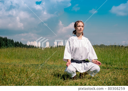 teenage girl karateka before starting training outdoor enters the mokuso meditative state in the seiza pose 80308259