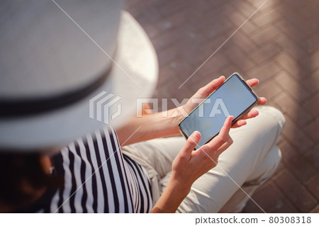 A woman wearing a protective mask looks at her smartphone display 80308318